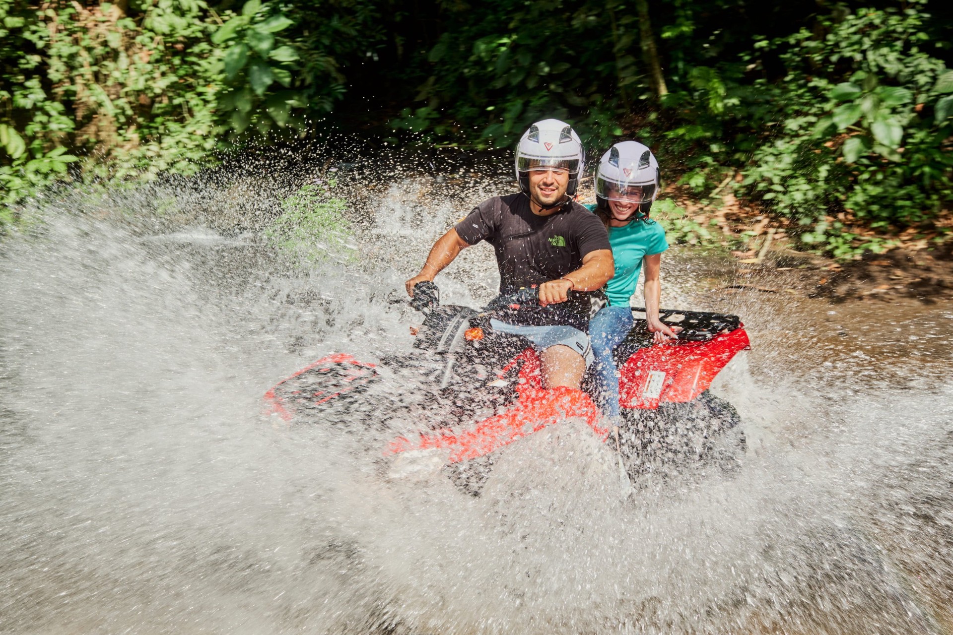 Couple on a red ATV mid river splash in the Costa Rican rainforest